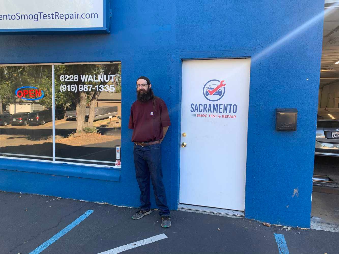 A man is standing in front of a blue building of Sacramento Smog Test and Repair