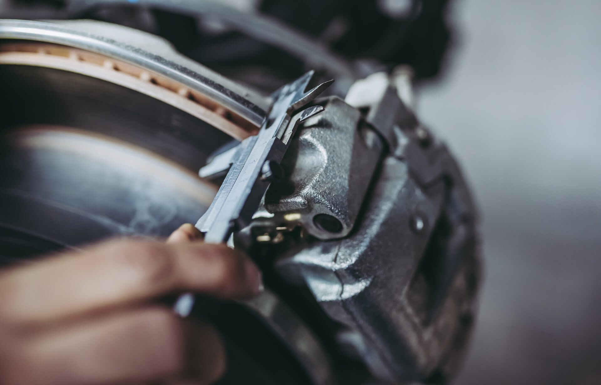 A person is working on a brake caliper with a pair of pliers at Sacramento Smog Test and Repair