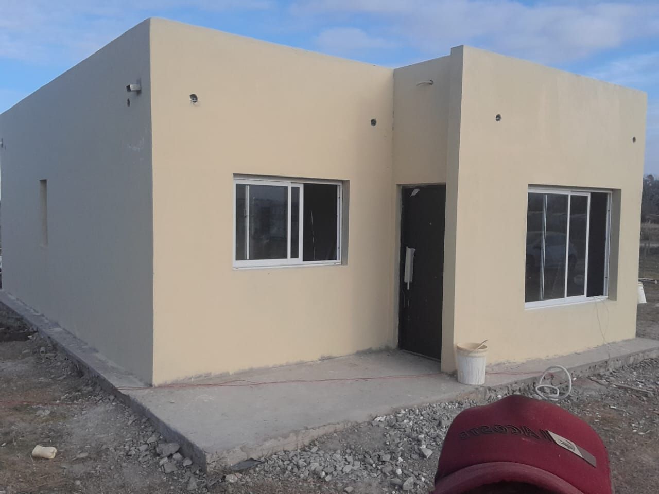 Casa de una sola planta, de color tostado, con ventanas de marco blanco, puerta negra y patio de hormigón 