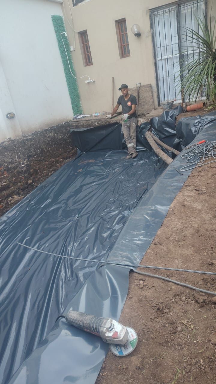 Un operario instala una lámina impermeabilizante negra en una zona excavada para un proyecto.