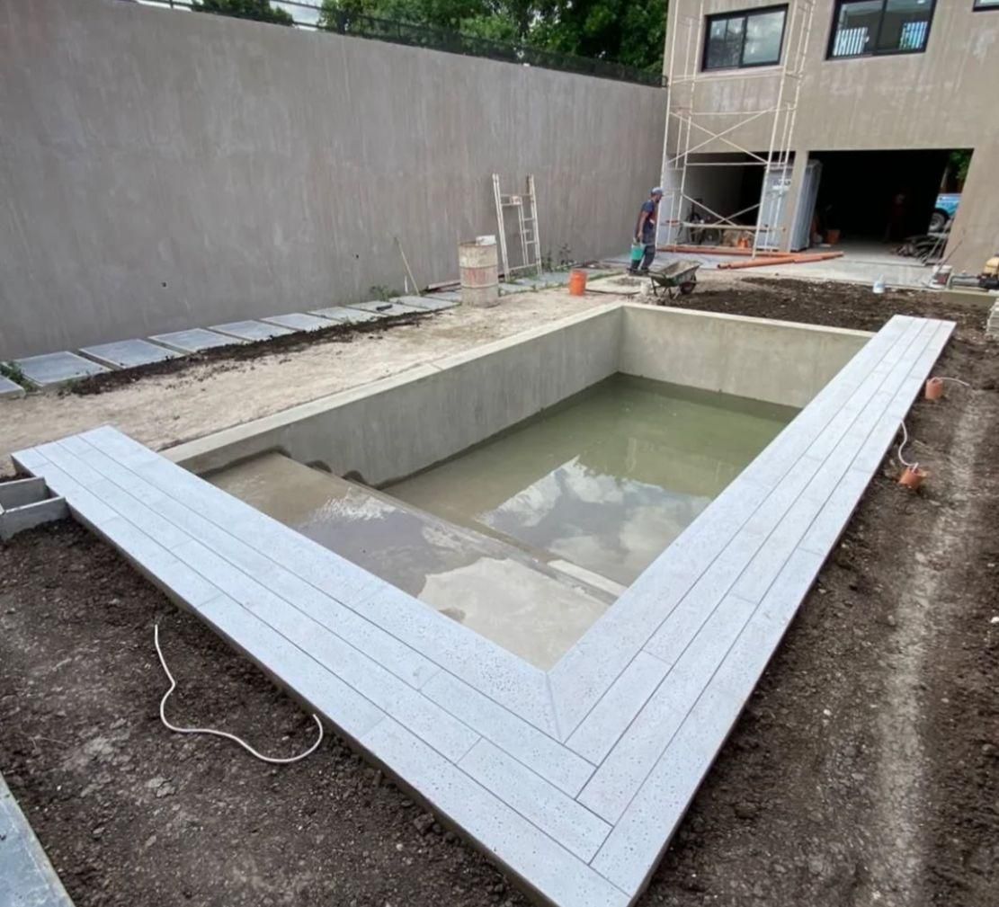 Zona en construcción con una piscina parcialmente construida, rodeada de tarima gris y muros de hormigón.