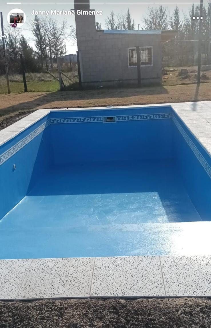 Piscina rectangular azul vacía con borde moteado; pequeño edificio al fondo.