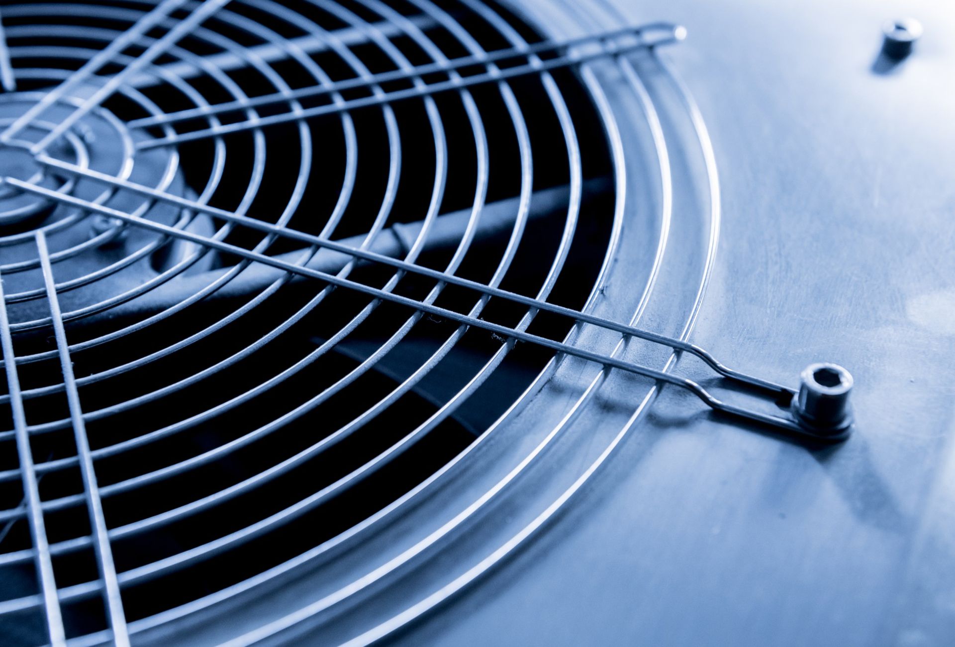Close-up of a metal fan grille with a central hub on a blue-tinted surface