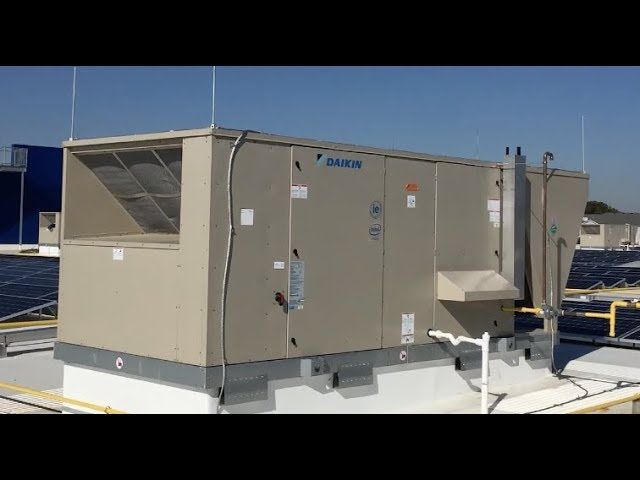 Rooftop HVAC unit in beige metal casing on a flat roof under a clear blue sky
