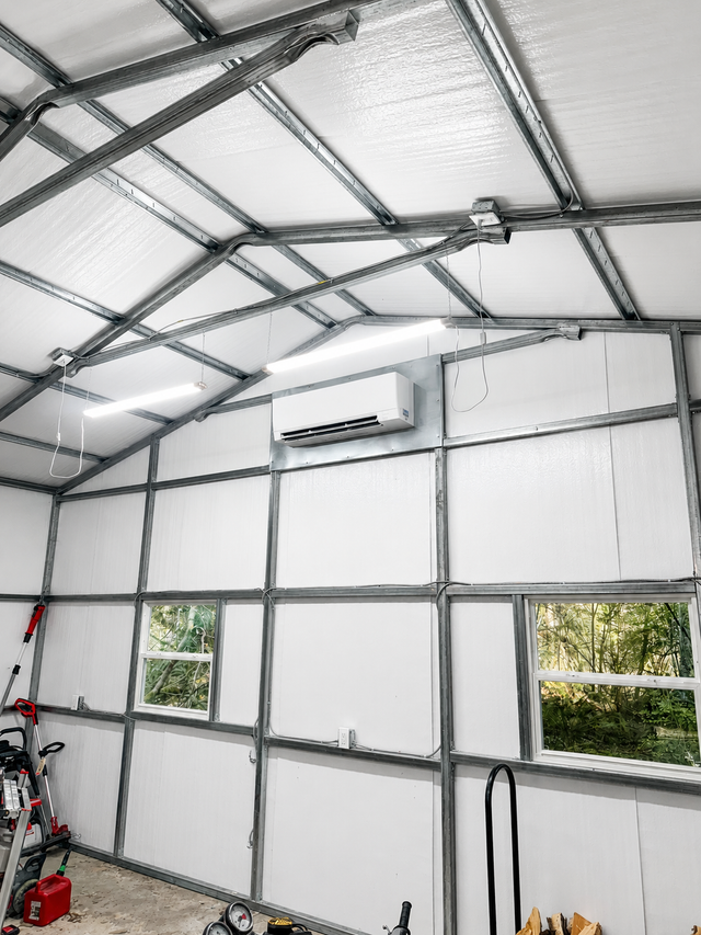 Small insulated workshop interior with metal frame walls, white panels, windows, and a wall-mounted air conditioner