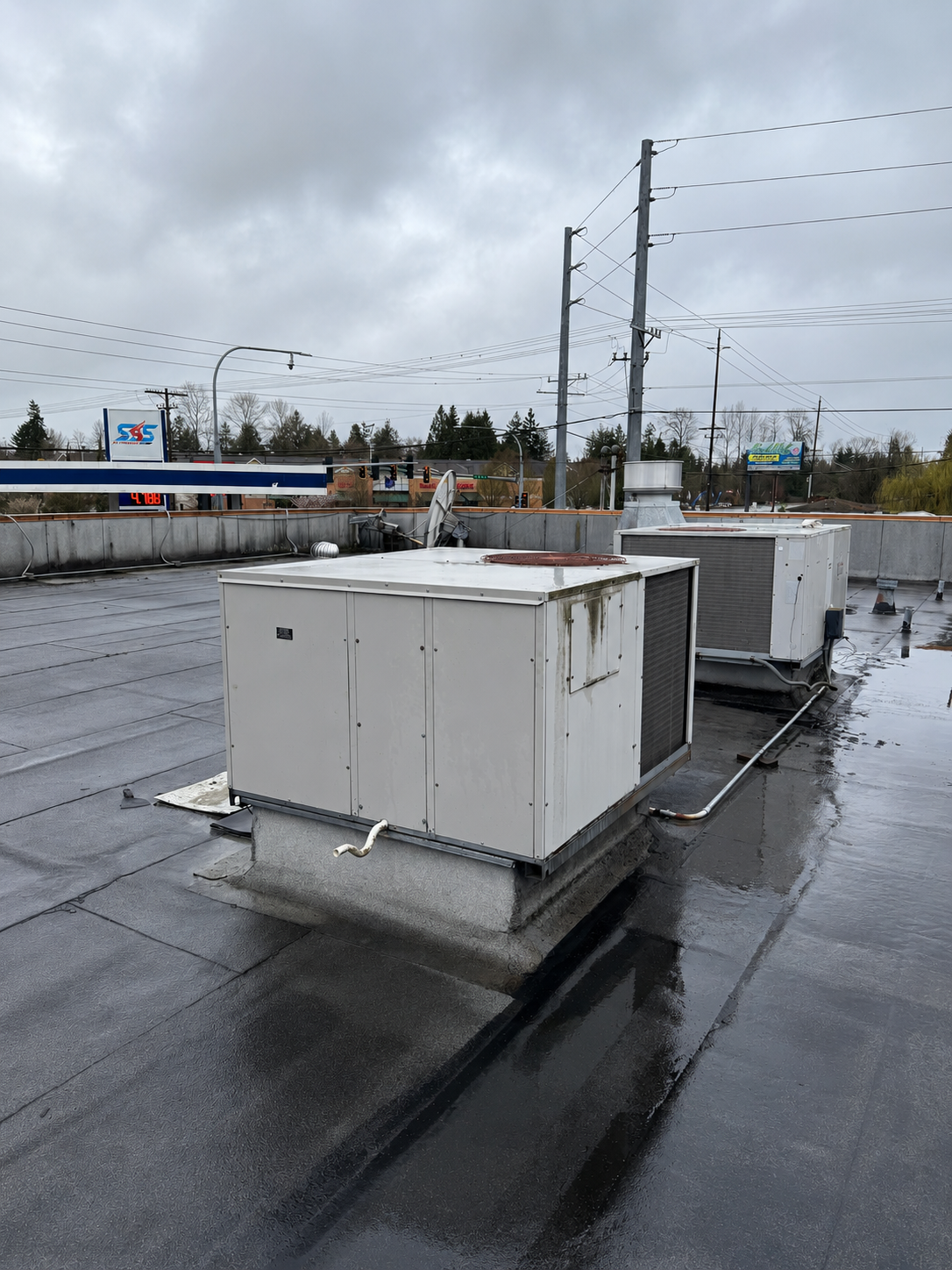 Rooftop HVAC units on a wet flat roof under an overcast sky.