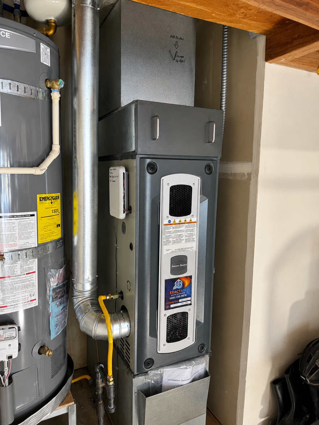 Utility room with a water heater, gray furnace, and exposed pipes and vents.