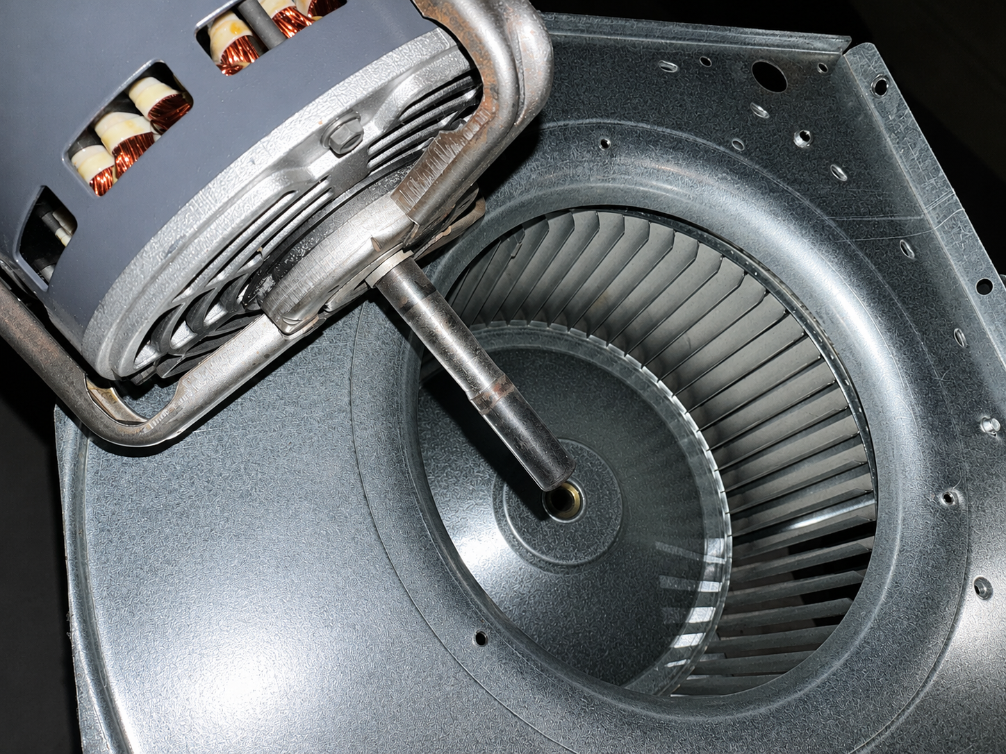 Close-up of a damaged centrifugal fan motor with exposed copper windings inside a metal housing