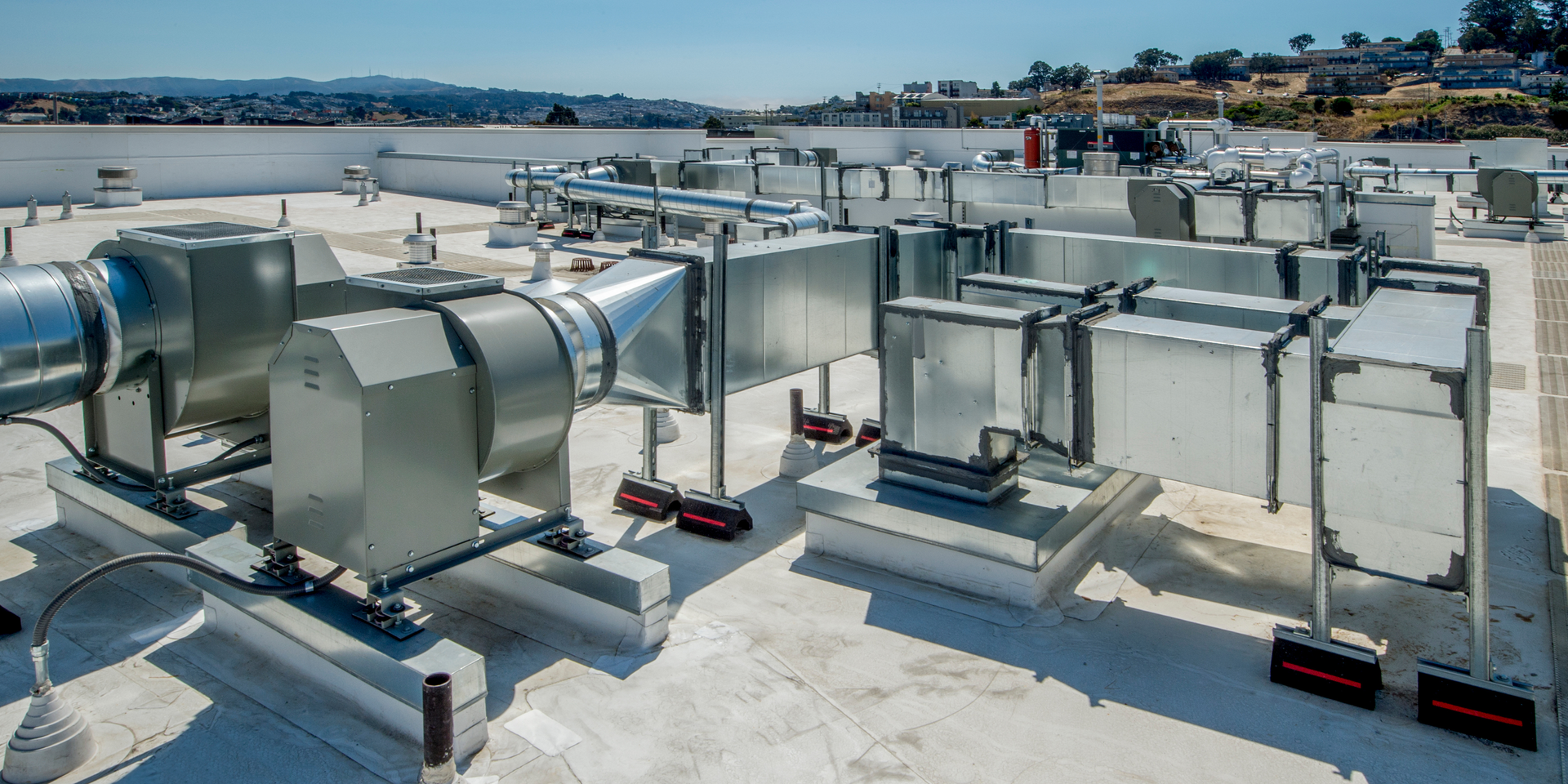 Rooftop HVAC ventilation units and ducts on a flat industrial roof under a clear sky