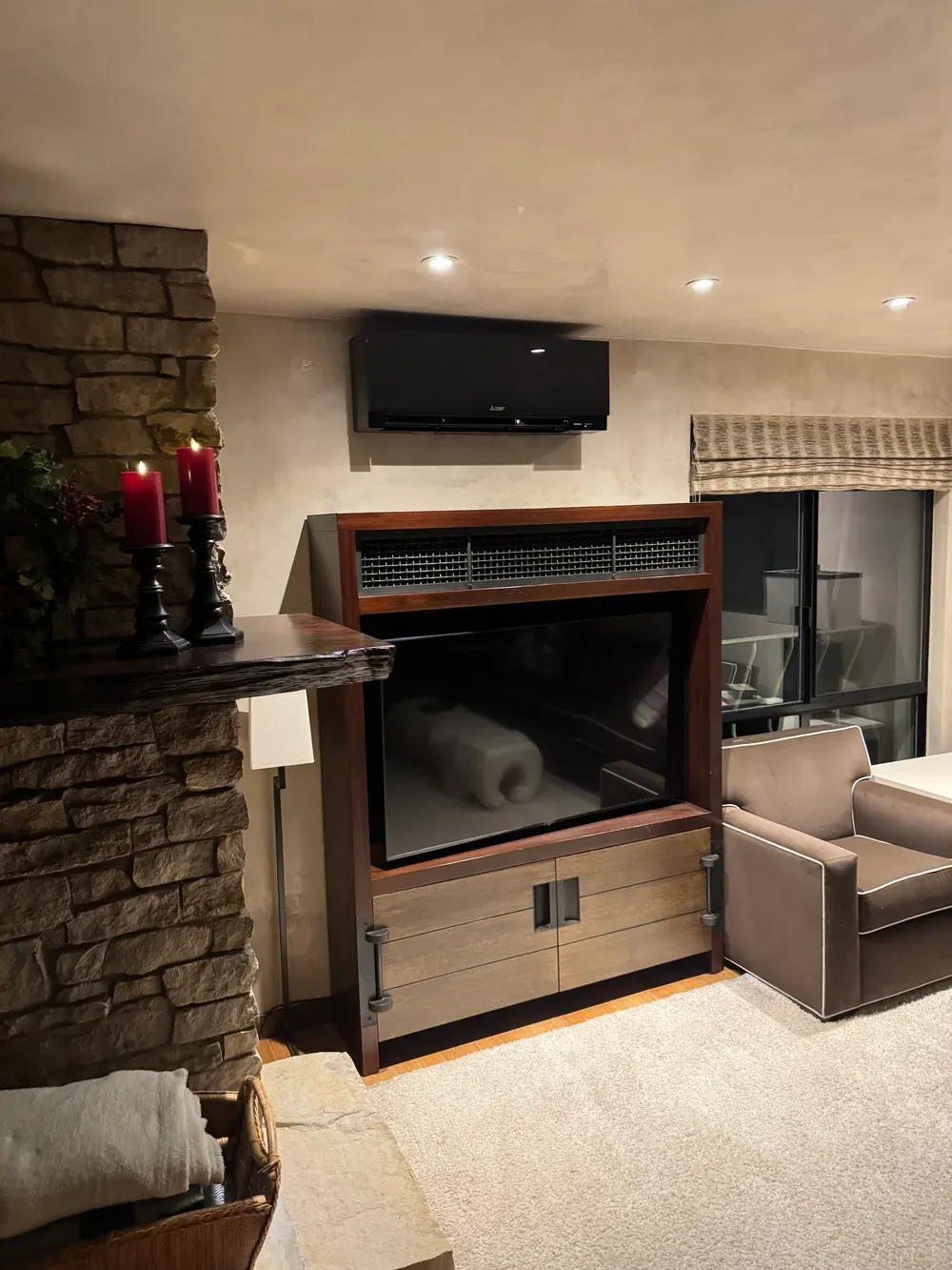 Living room with stone fireplace, built-in TV cabinet, and tan armchair by a window