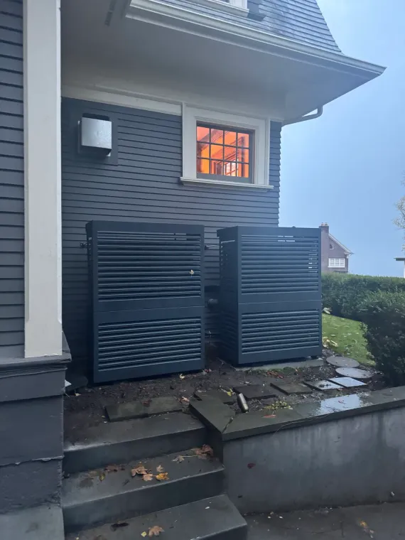 Dark house exterior with black slatted gate, lit window, and stone steps by a hedge