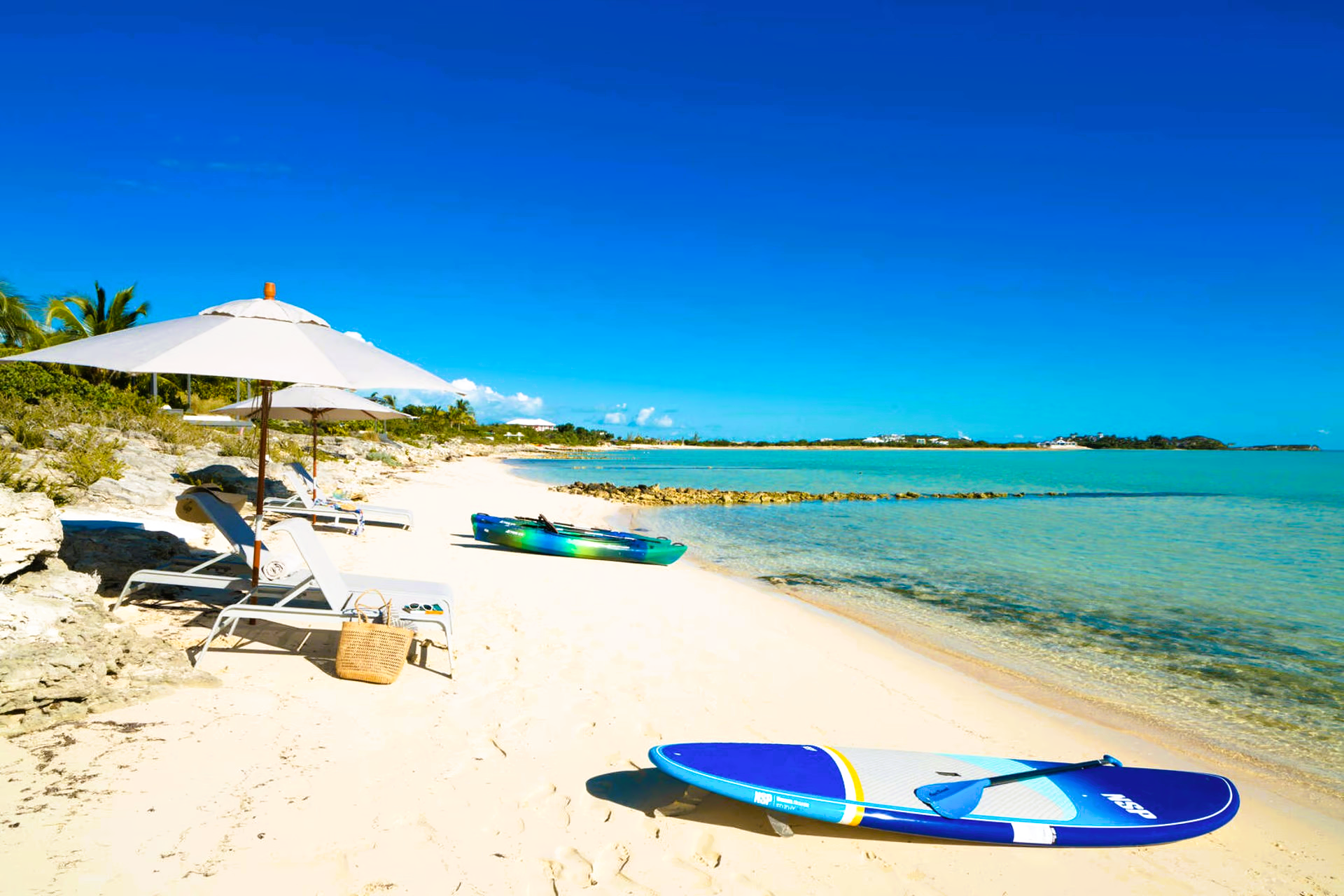 A beach with chairs and umbrellas and a surfboard on the sand