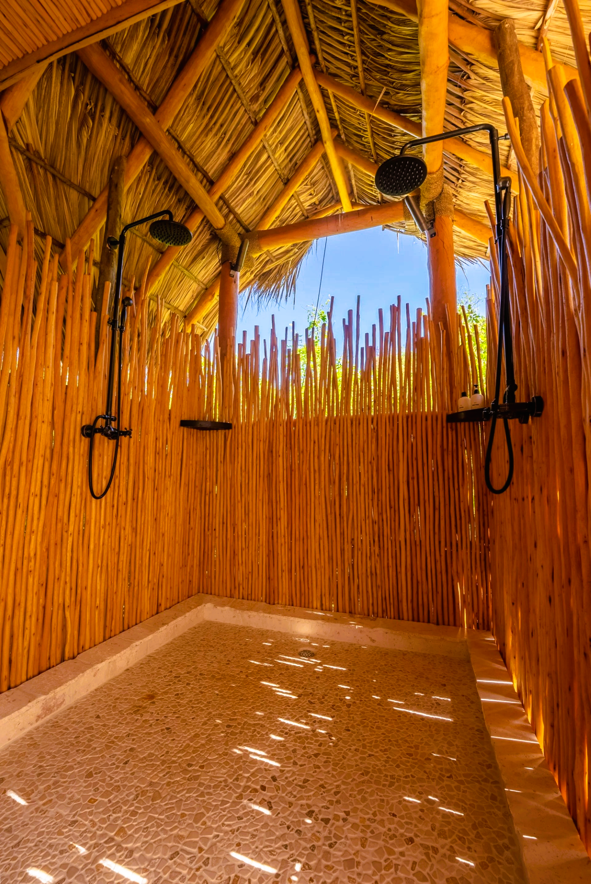 A wooden shower with two shower heads and a thatched roof.