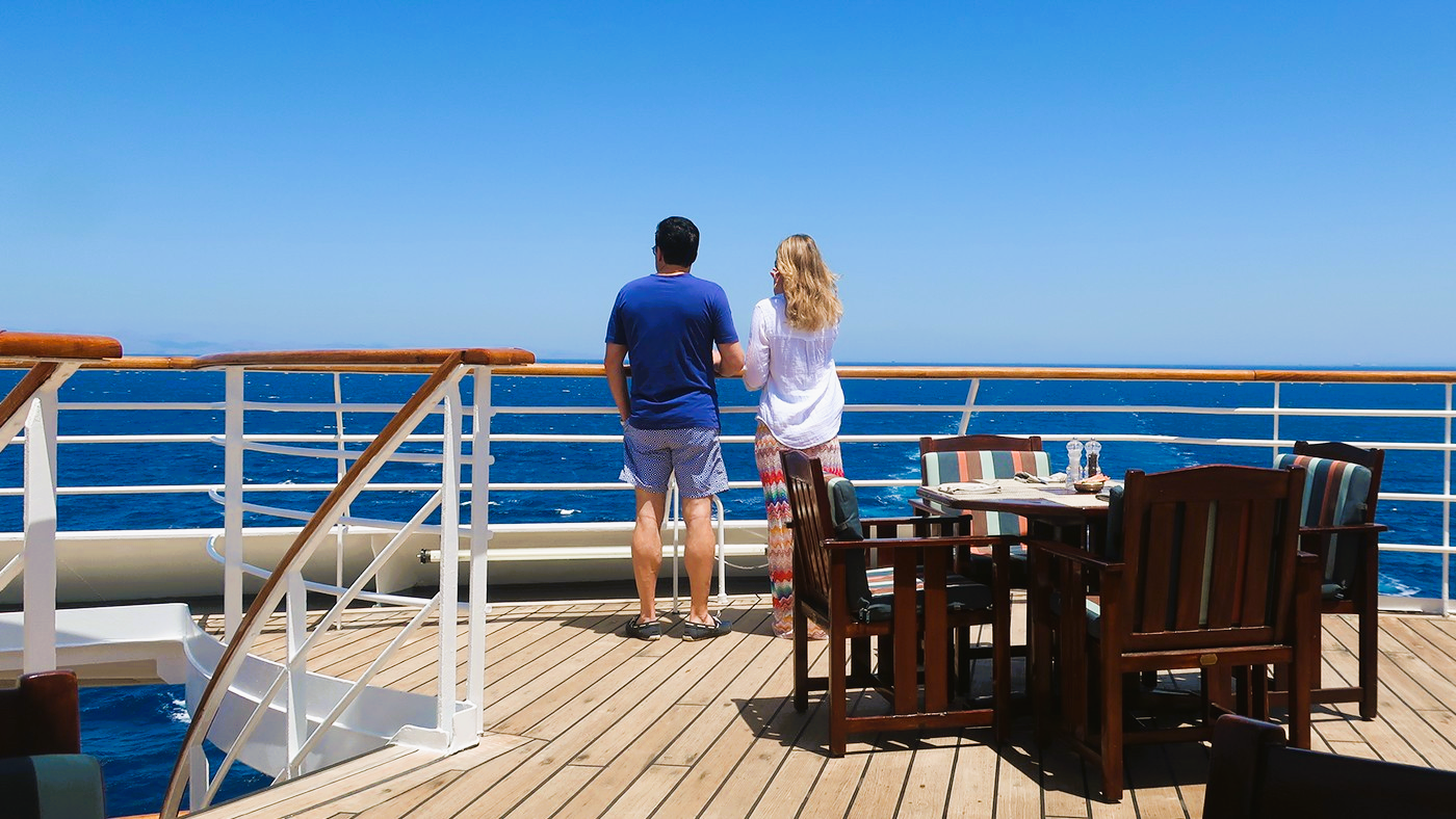 A man and a woman are standing on the deck of a cruise ship looking at the ocean.