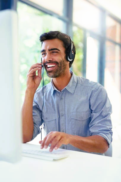 Man with headset smiling while typing at computer.
