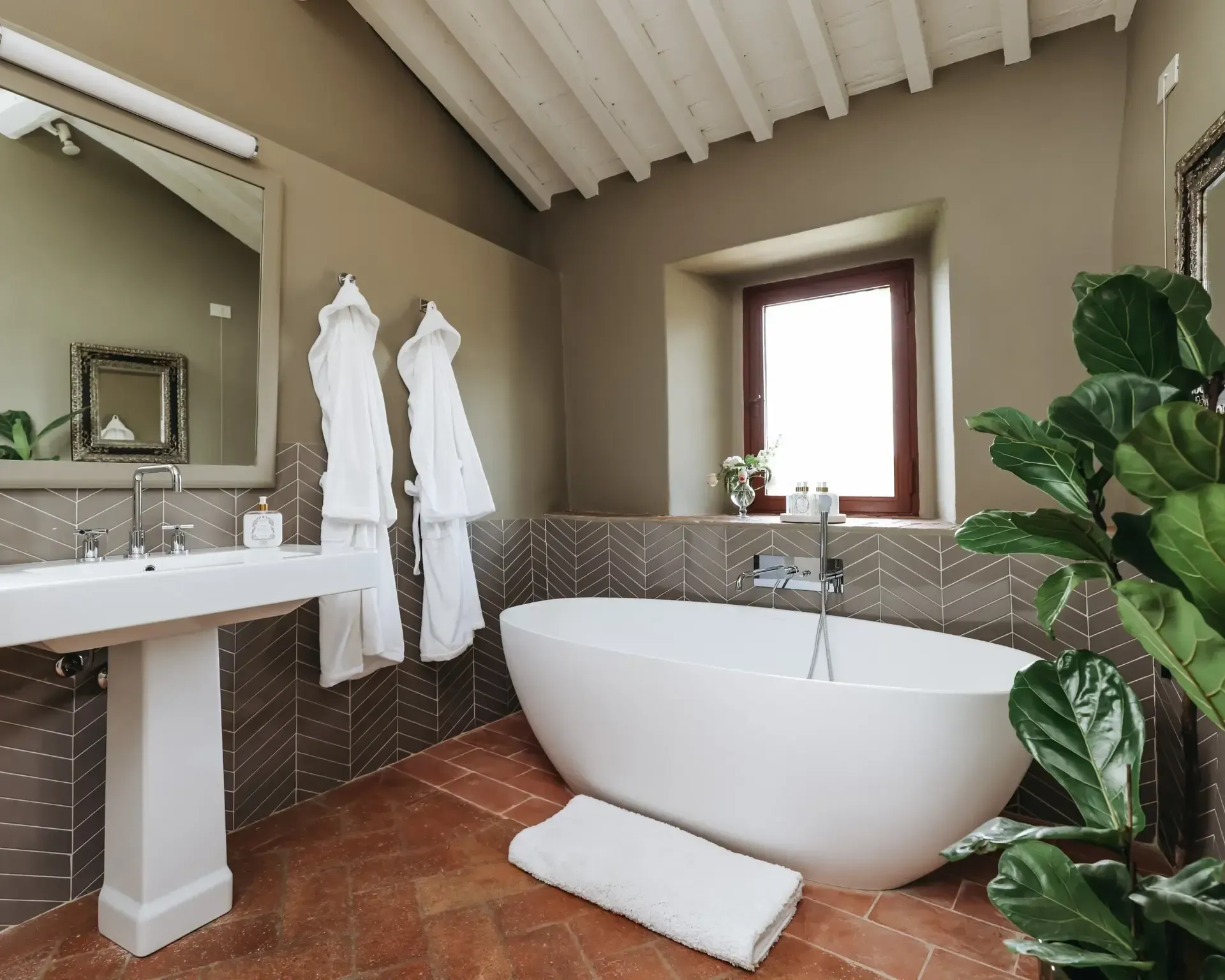 Bathroom with white tub, sink, and robes. Brown brick floor and green walls.