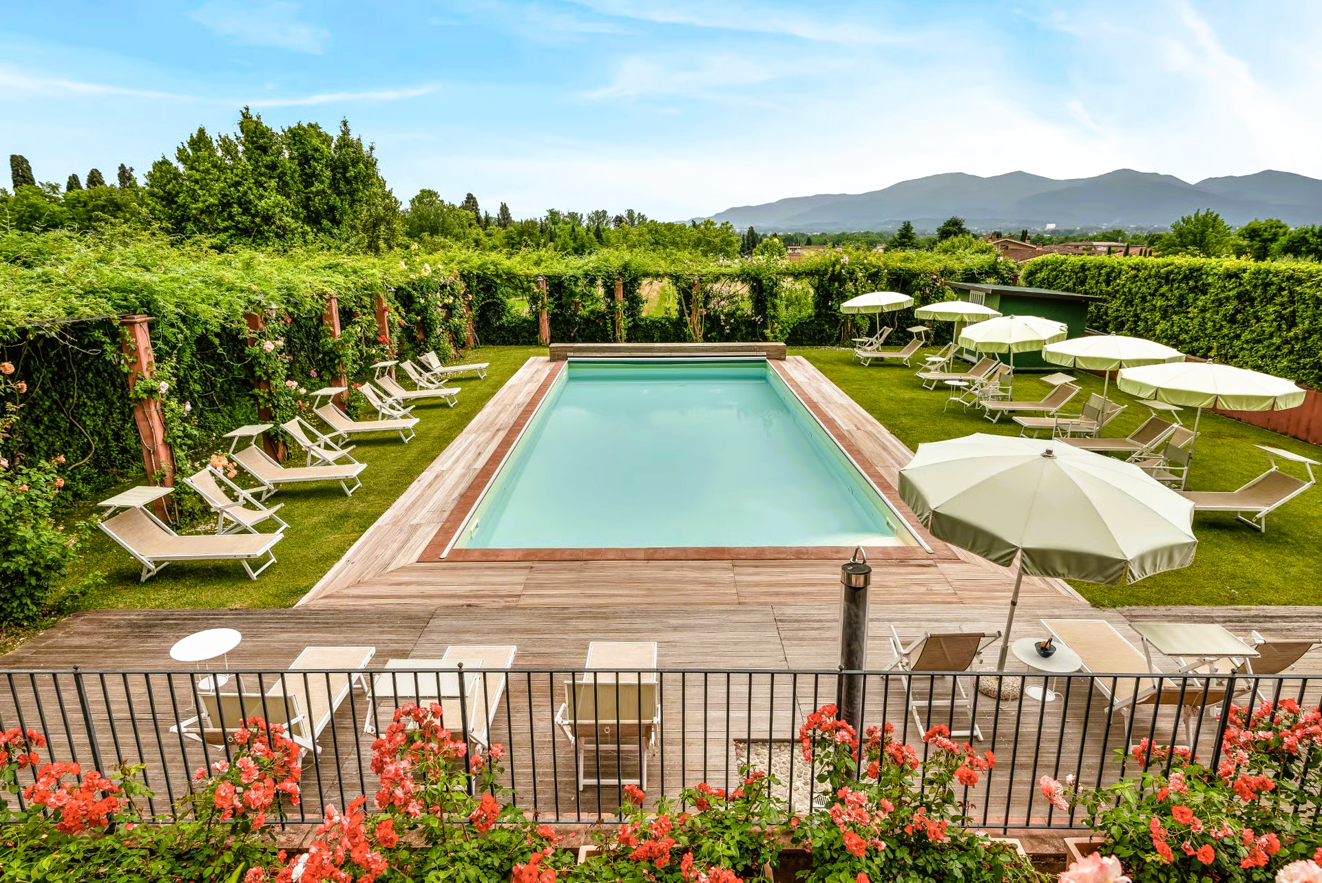 Pool surrounded by lounge chairs, umbrellas, and lush greenery. Mountains in the distance.