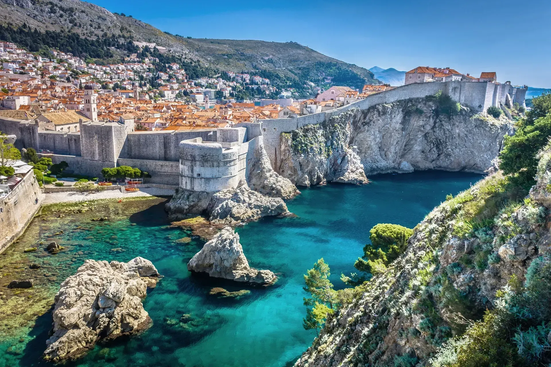 City walls and buildings on a cliff overlooking the turquoise Adriatic Sea in Dubrovnik, Croatia.