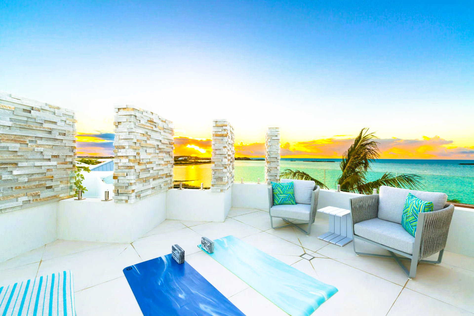 A balcony with chairs and a yoga mat overlooking the ocean.