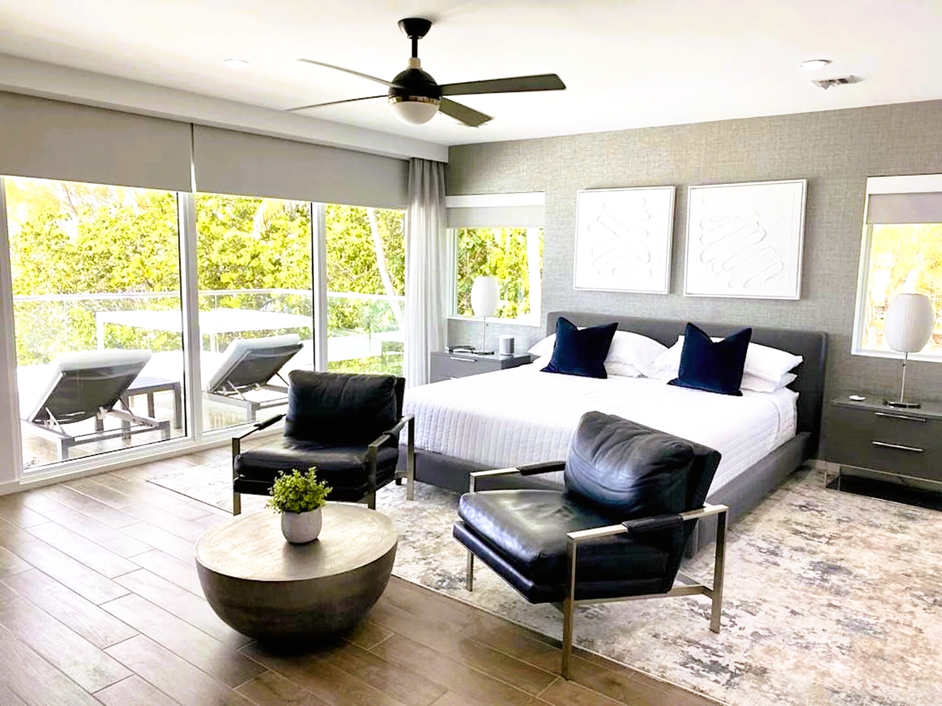 A bedroom with a large bed , two chairs , a coffee table and a ceiling fan.
