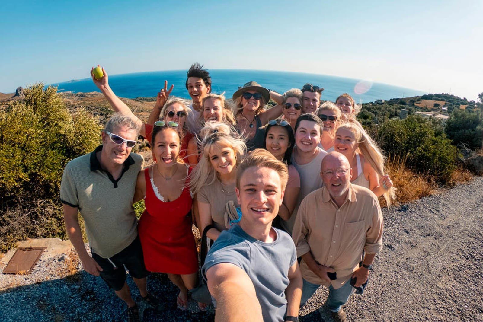 Group of smiling people taking a selfie outdoors with blue ocean in background.