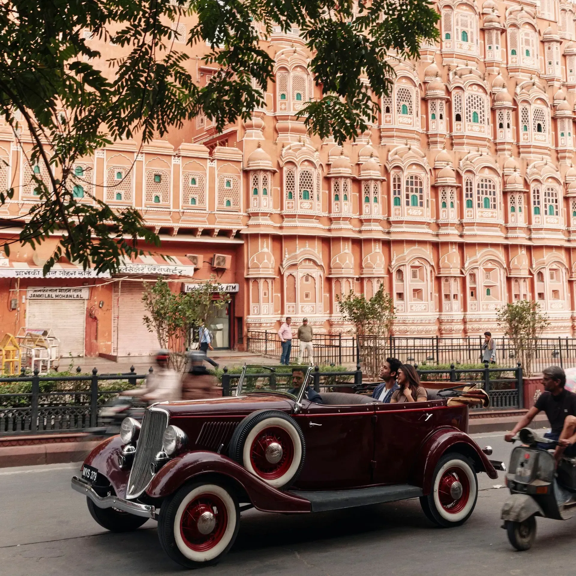 Vintage maroon car on a street in front of the pink Hawa Mahal palace, Jaipur, India.
