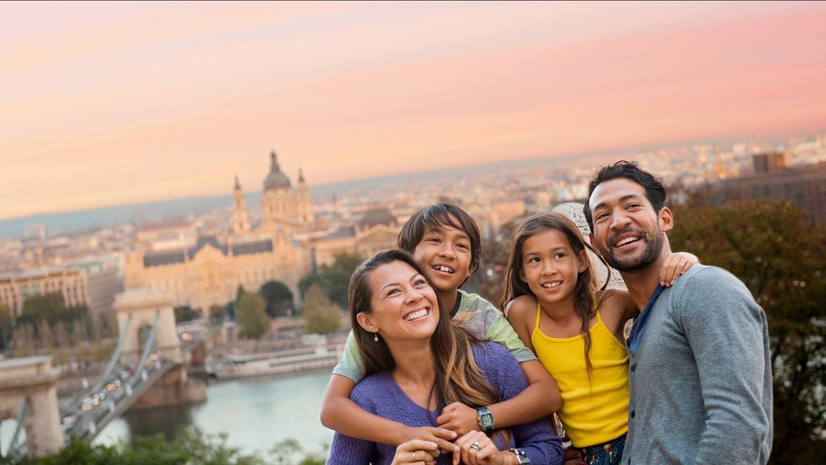 Family smiling and embracing, overlooking a cityscape at sunset.