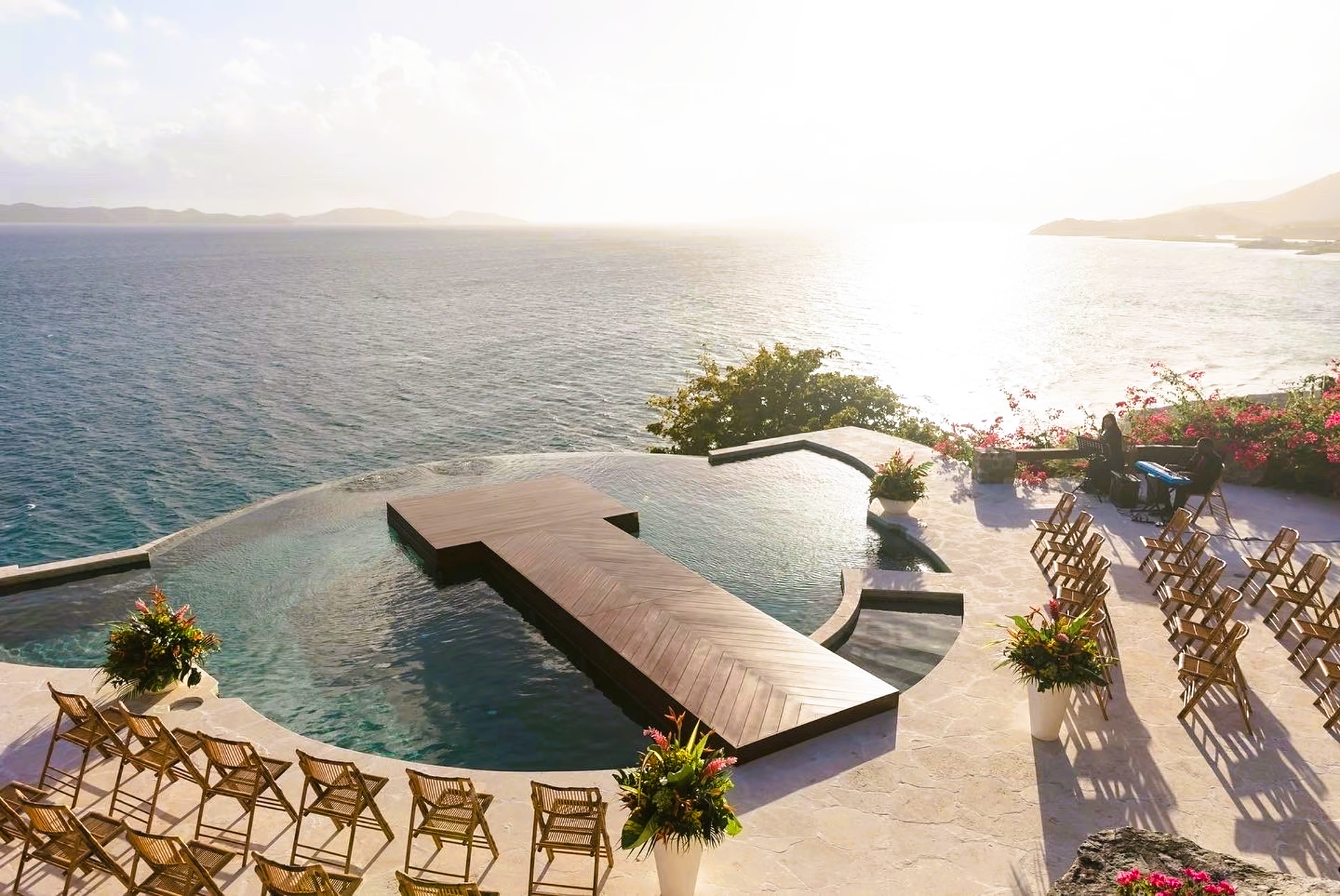 A wedding ceremony is taking place in front of a swimming pool overlooking the ocean.