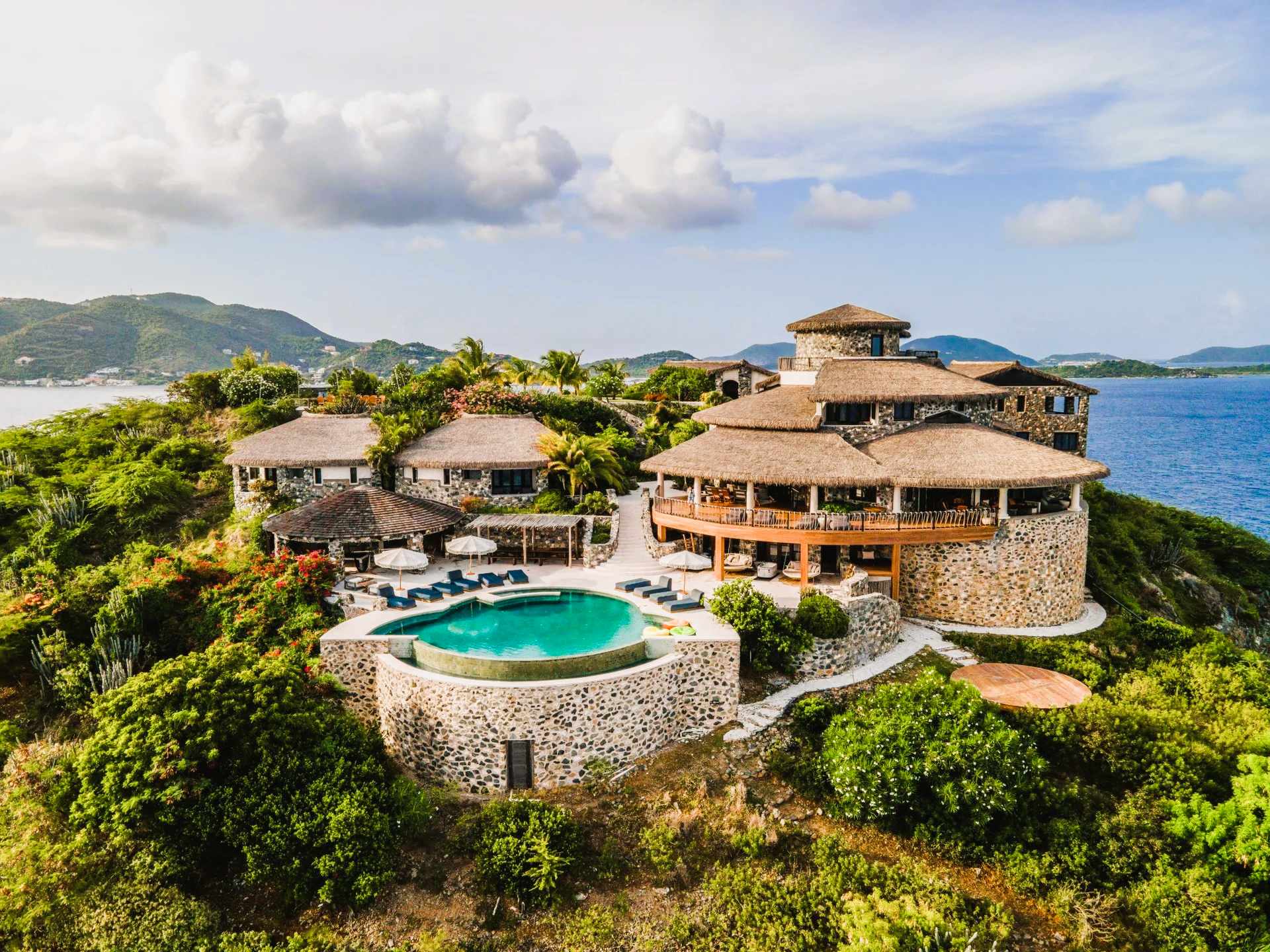 An aerial view of a large house on top of a hill overlooking the ocean.