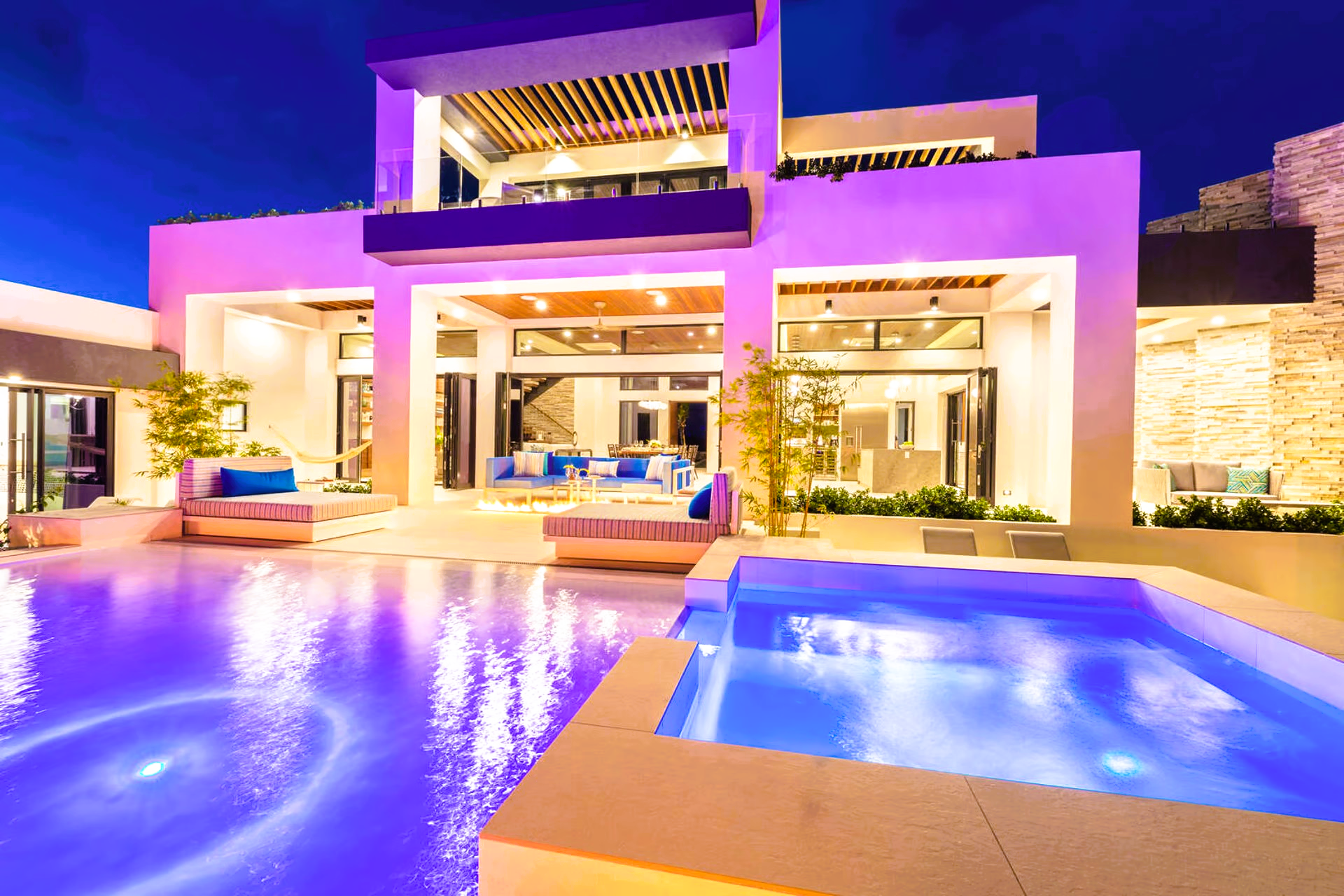 A large house with a swimming pool in front of it at night.