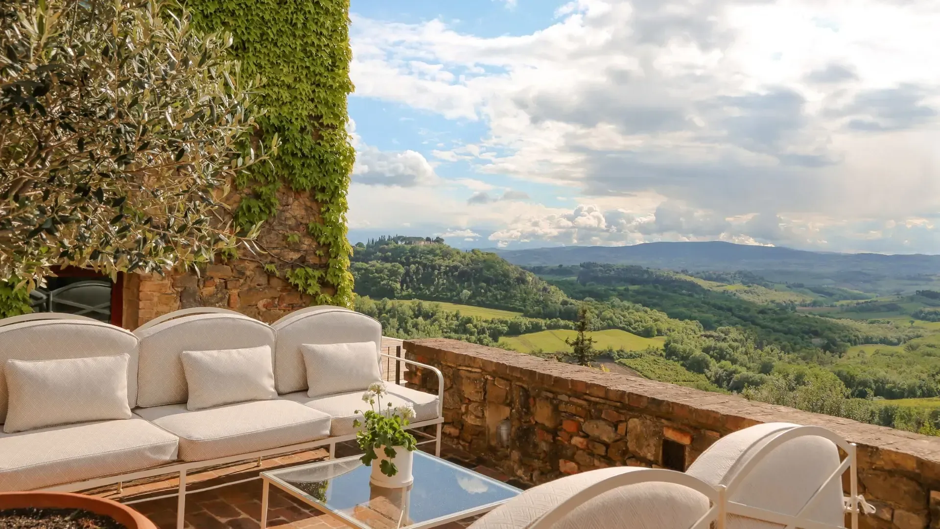 Outdoor seating with a white couch, overlooking rolling green hills under a cloudy sky.