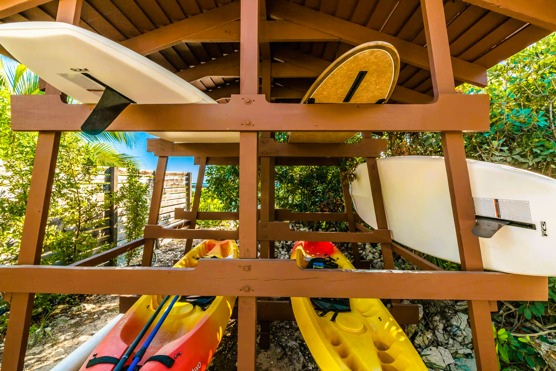 Kayaks and surfboards are stacked on top of each other on a wooden rack.