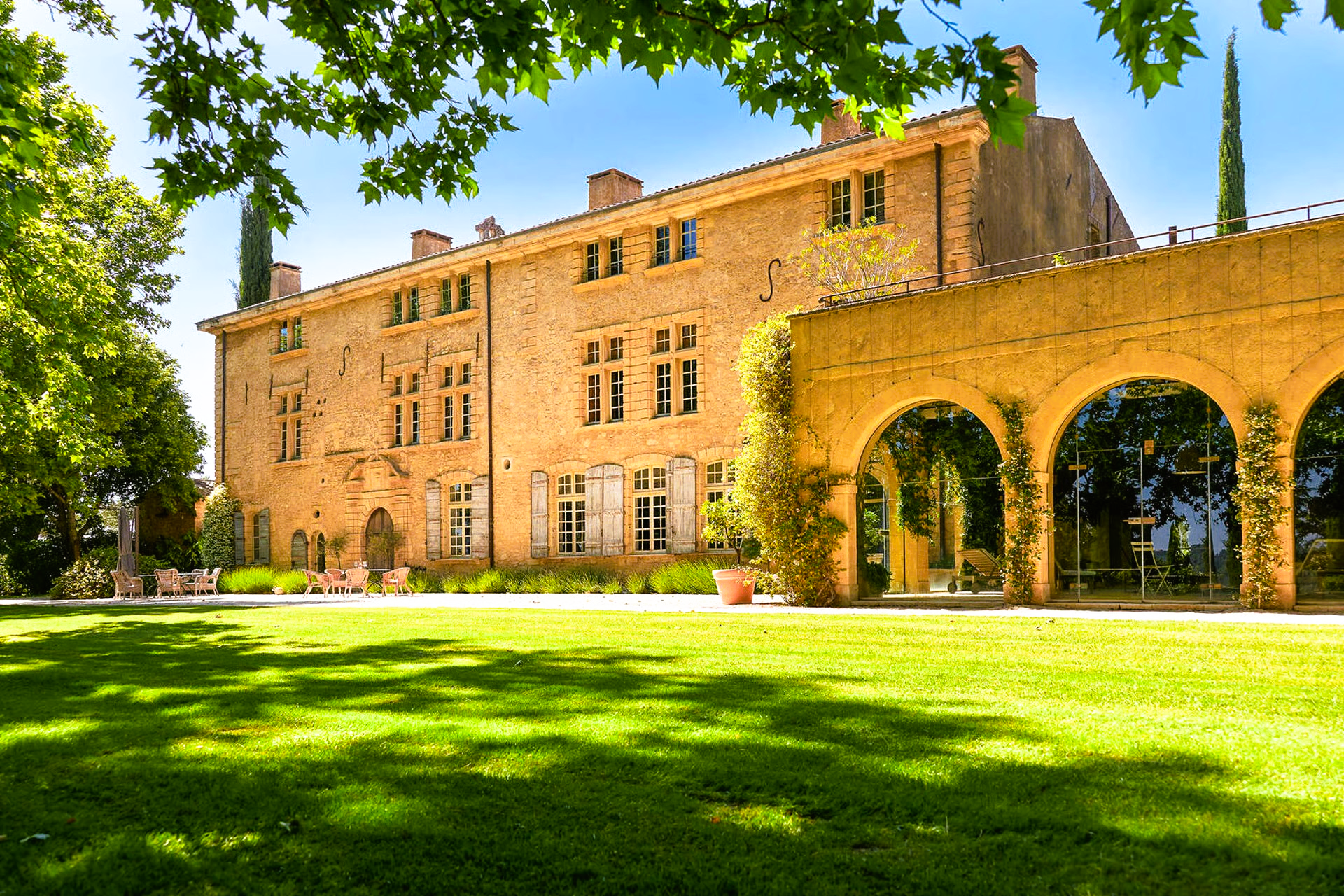 Large stone manor house with arched walkway and green lawn.