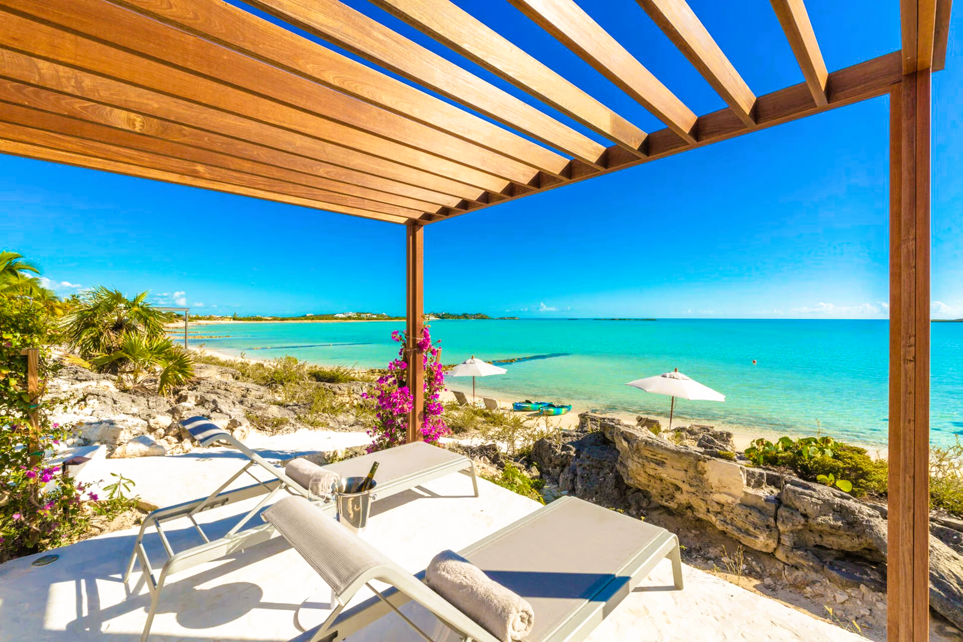 A pergola overlooking the ocean with lounge chairs and umbrellas.