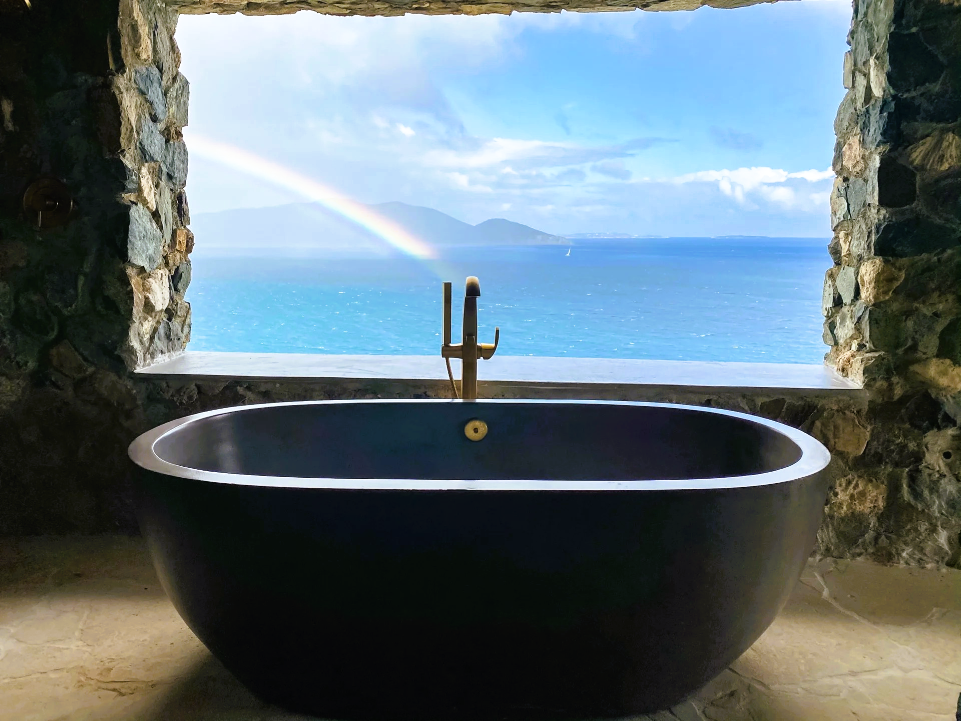 A black bathtub is sitting in front of a window overlooking the ocean.