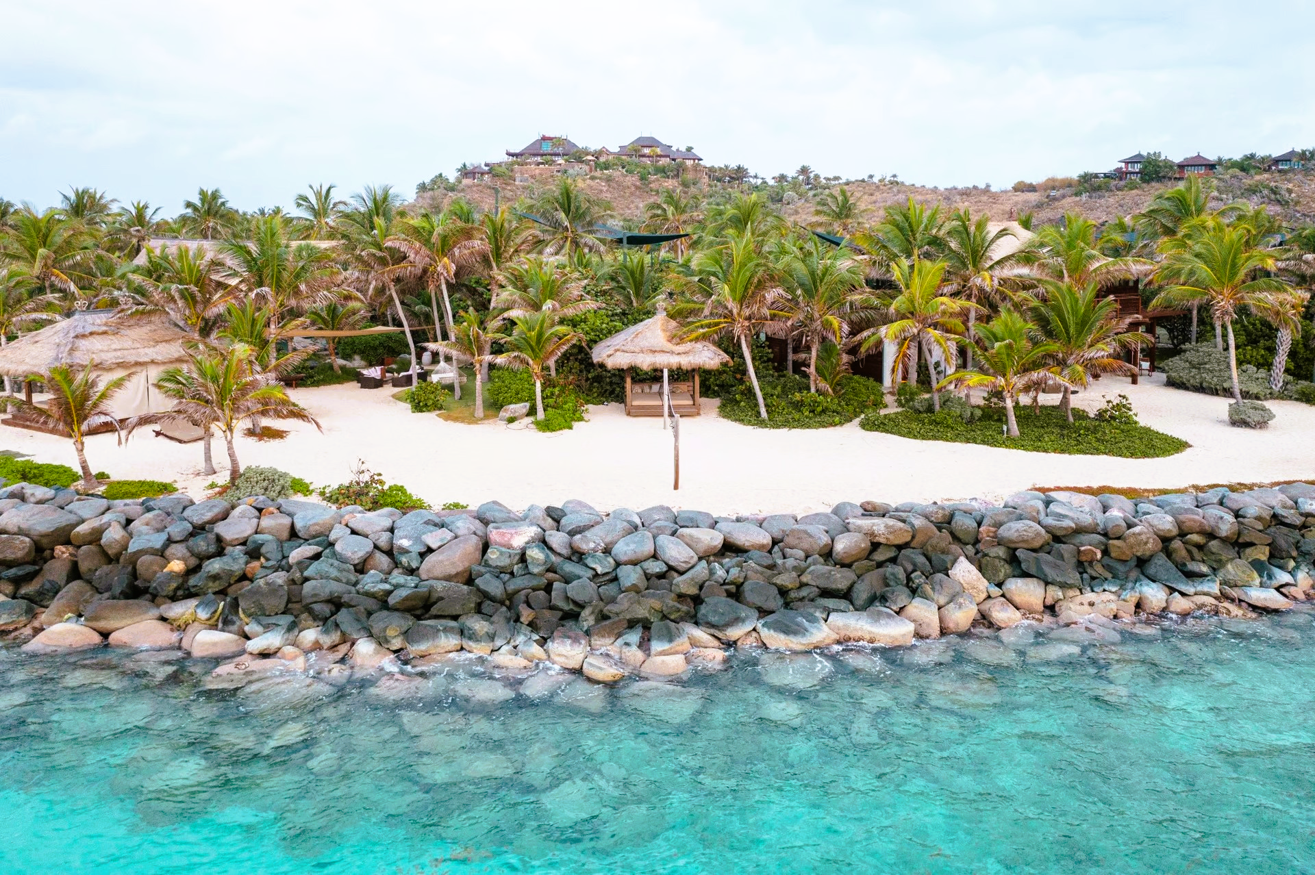 An aerial view of a tropical beach with palm trees and a rock wall.
