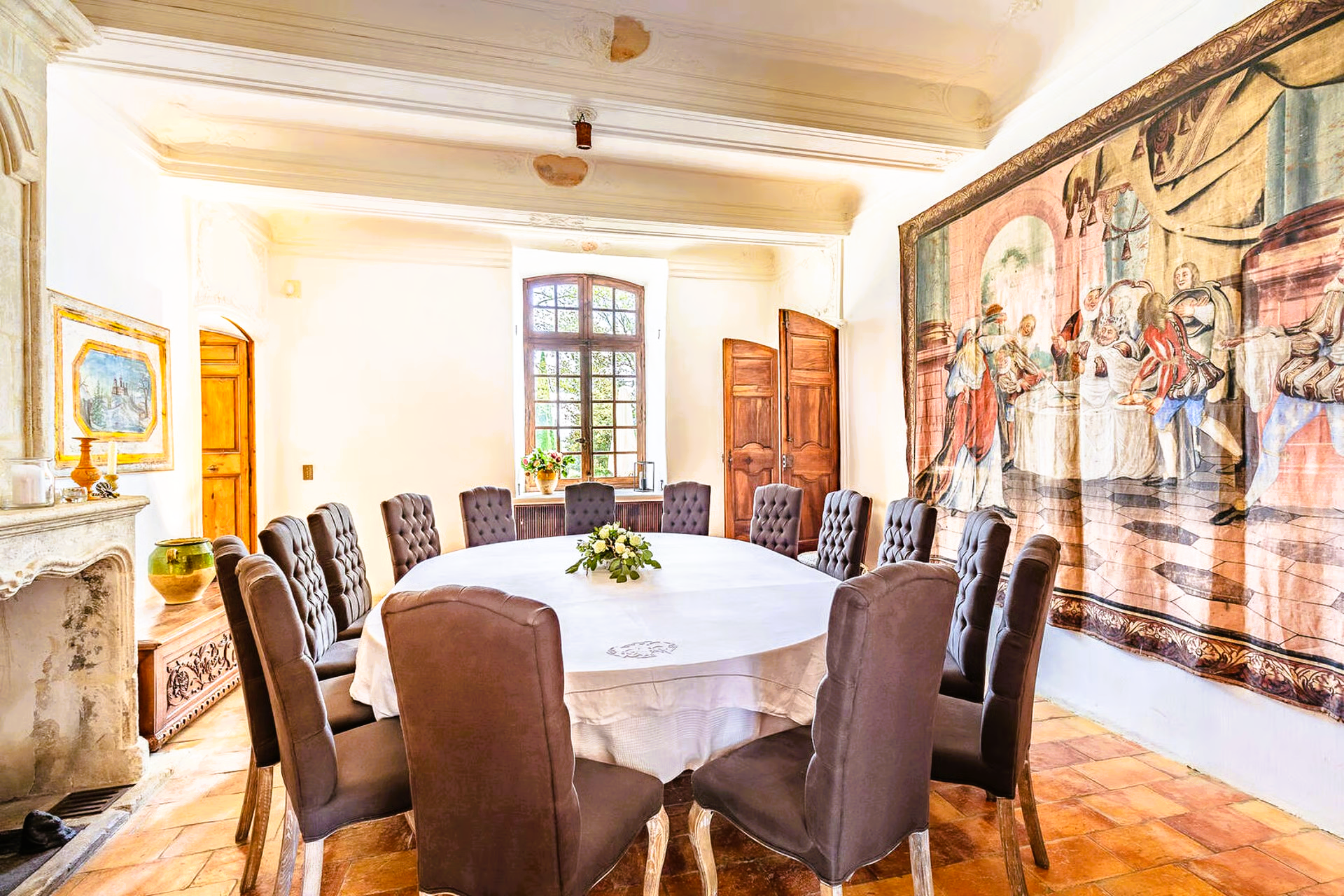 Elegant dining room with a large round table set for a meal. A tapestry adorns the wall.