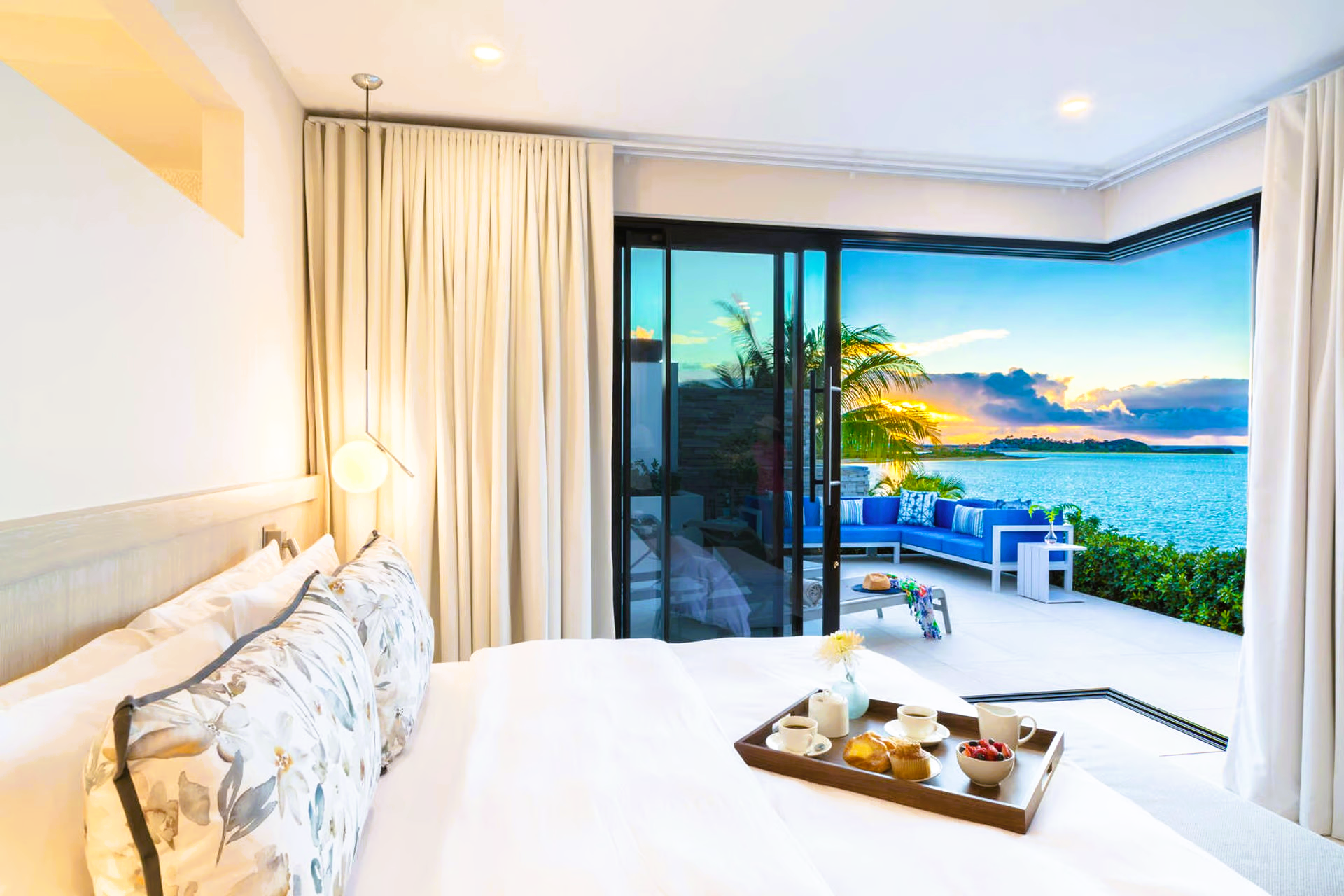 A bedroom with a tray of food on the bed and a view of the ocean.