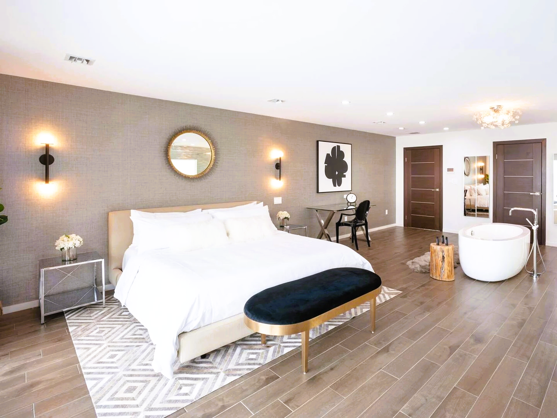 A bedroom with a large bed , bathtub , desk and mirror.