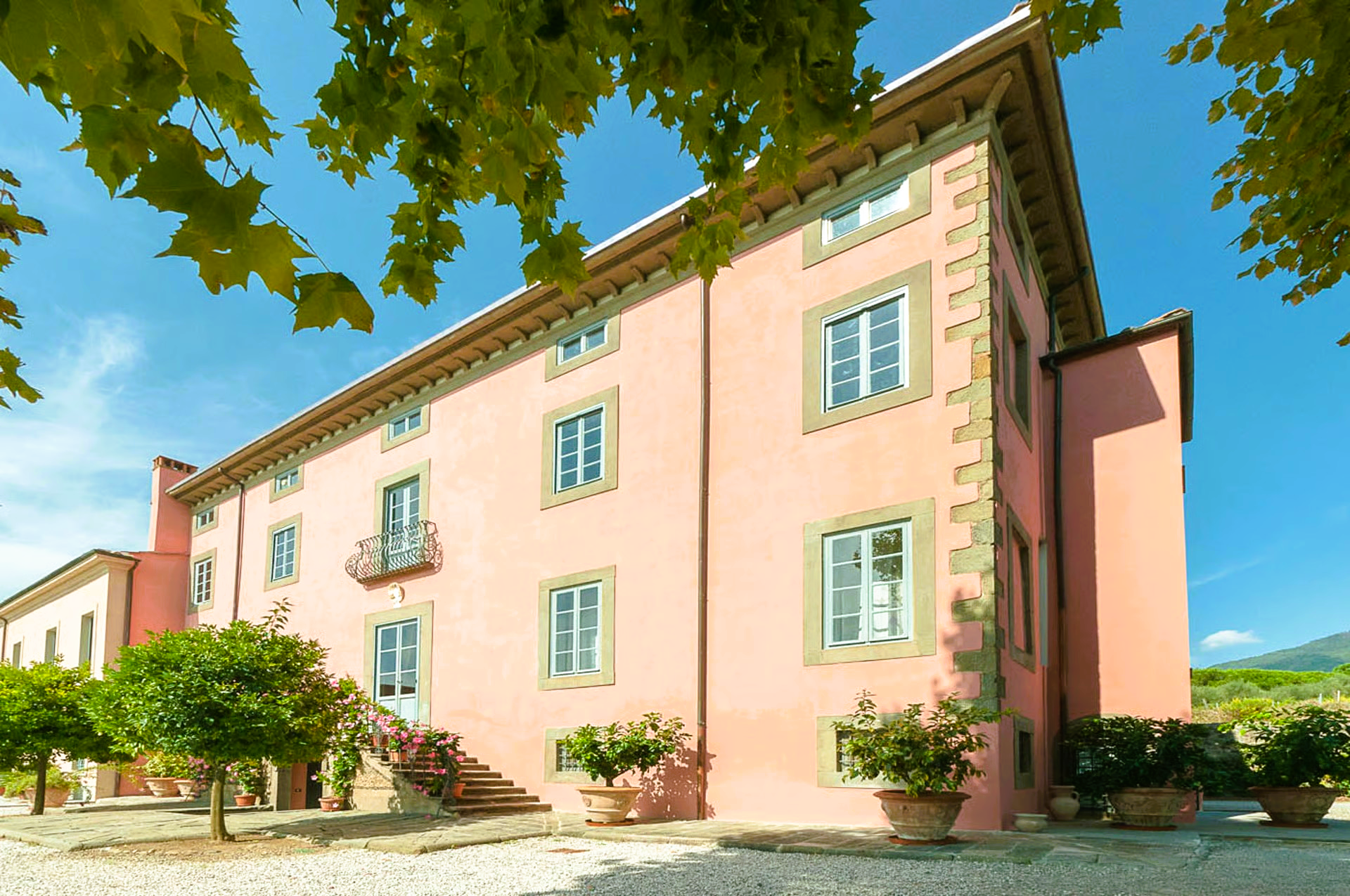 Pink stucco building with light stone trim, trees, and blue sky.