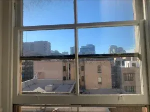 View from a window of city buildings under a blue sky. White window frame.