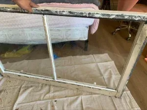 Wooden-framed window with two glass panes, resting on a drop cloth. Hand holds the top.