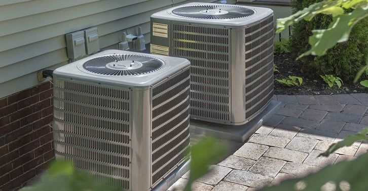 Two air conditioners are sitting on the side of a house.