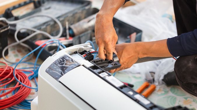 A man is fixing an air conditioner with a pair of pliers.