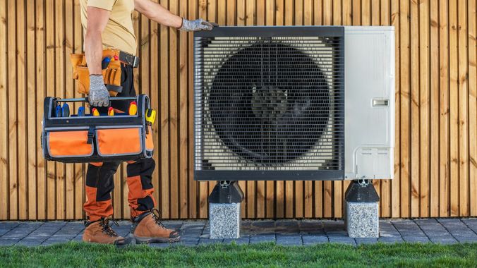 A man is holding a toolbox in front of an air conditioner.