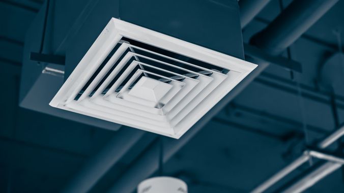 A square air vent is hanging from the ceiling of a building.