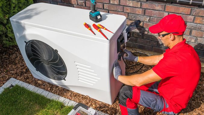 A man is working on a heat pump outside of a house.