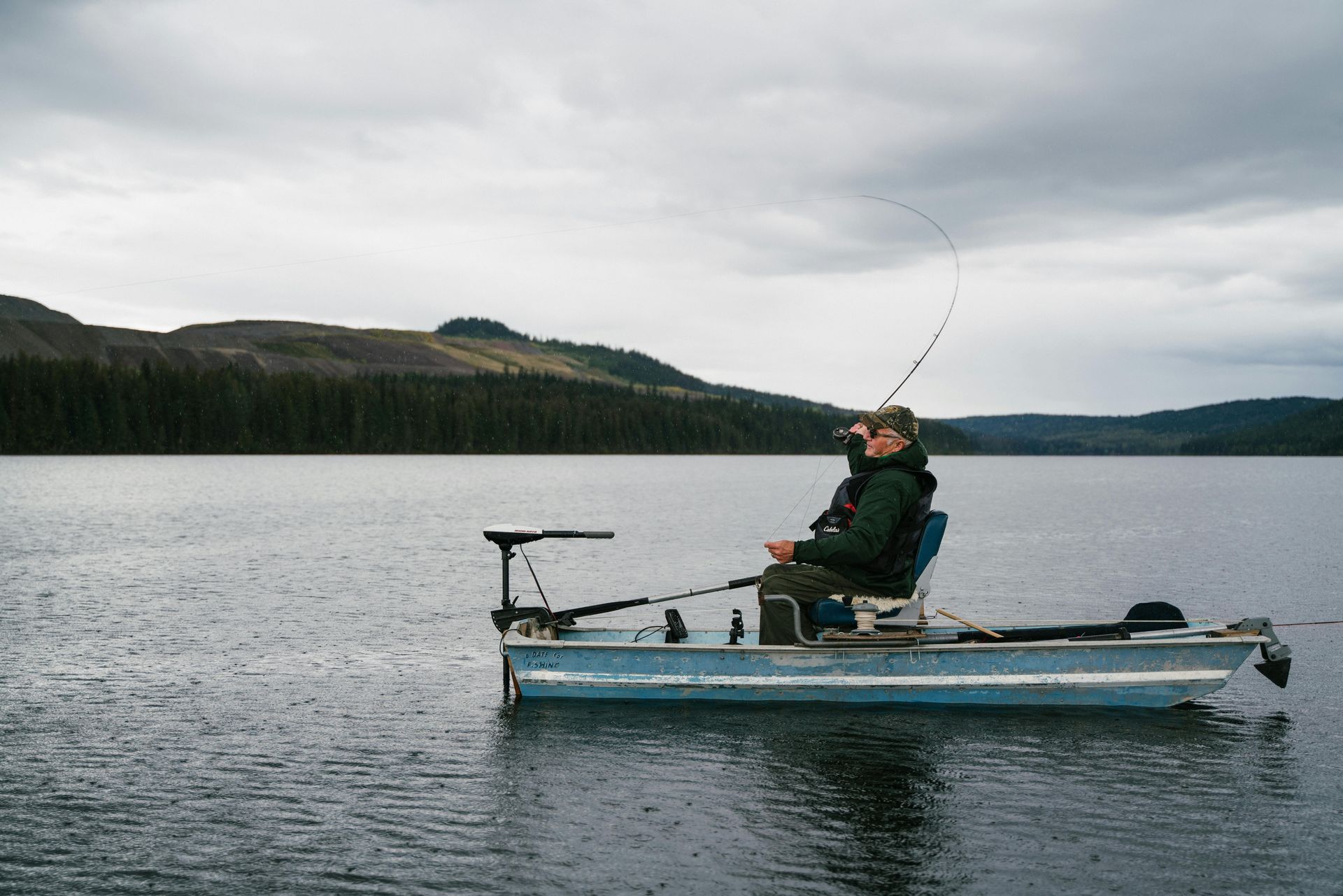 A man is fishing from a boat on a lake.
