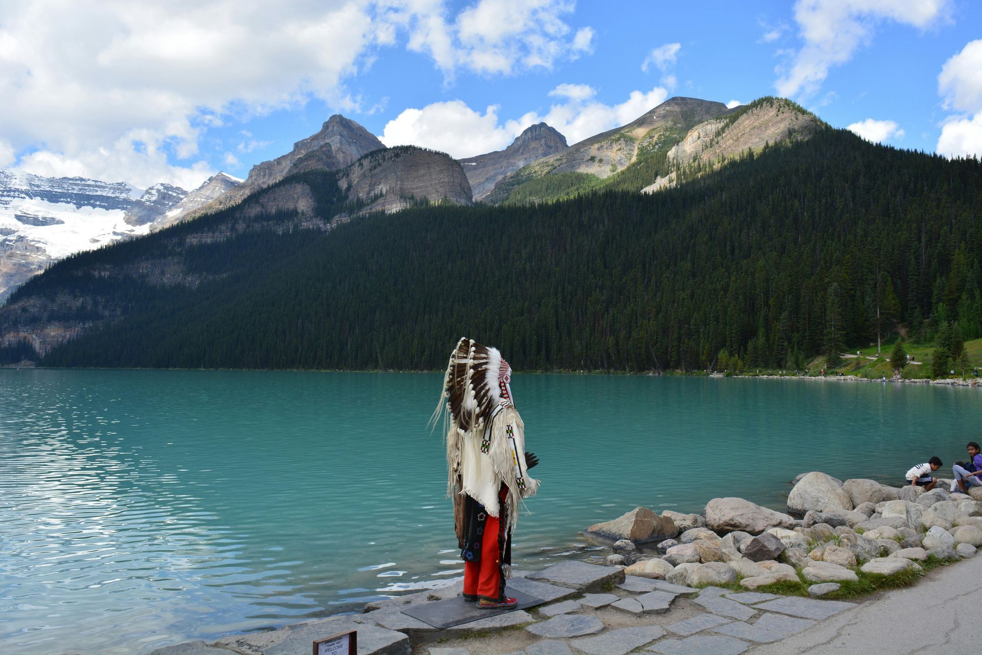 A person standing on the shore of a lake with mountains in the background