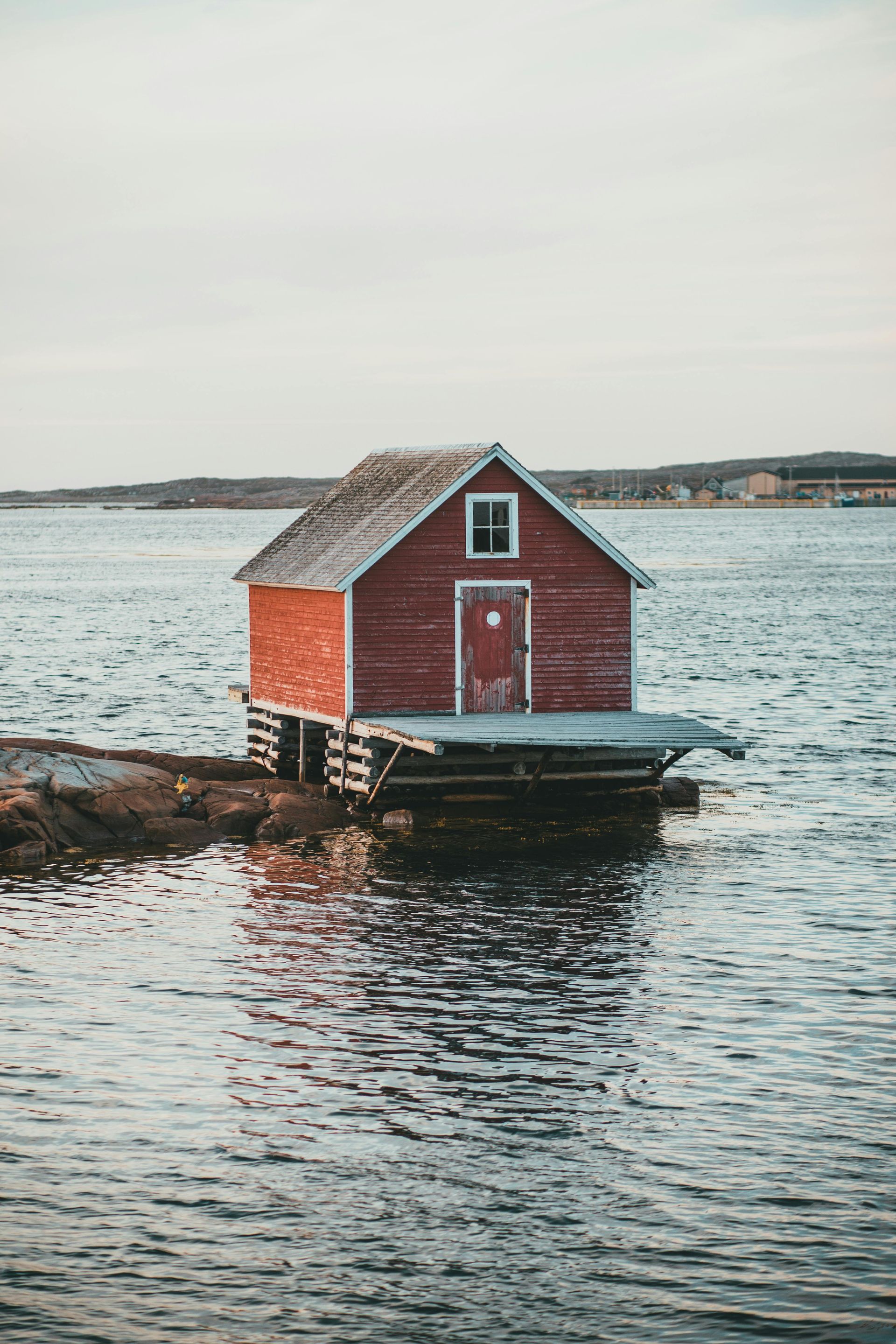 A small red house is floating in the middle of a body of water.